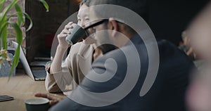 Multiracial group of men and women talking and drinking coffee sitting at table in cozy business cafe