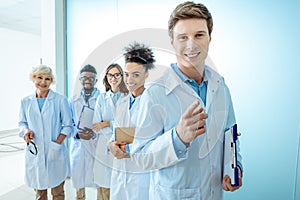 Multiracial group of smiling medical interns in lab coats standing in a row with clipboards