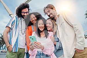 Multiracial group of young adult friends enjoying and smiling using a mobile phone app. Diverse buddies having fun