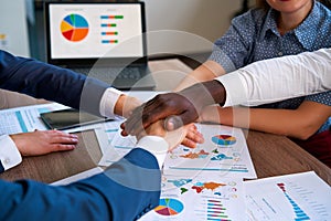 Multiracial hands come together over business charts in office, symbolizing teamwork, unity in diverse corporate group