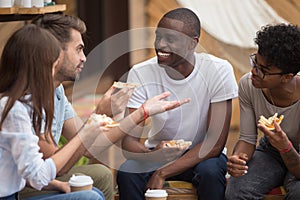 Multiracial happy friends laughing at joke eating pizza in cafe