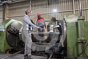 Multiracial Industrial Co-Workers Standing And Talking Next To Lathe Machine - Train Wheel Manufacturing