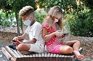 Multiracial kids using modern gadgets sitting outdoors