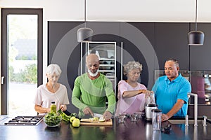 Multiracial male and female senior friends making healthy smoothie in kitchen at retirement home