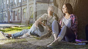 Multiracial male and female students sitting under tree, looking ahead, future