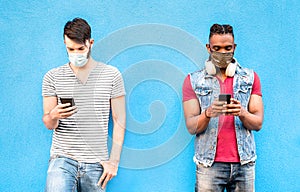 Multiracial male friends with face masks using tracking app with mobile smart phones - Young millenial people watching updates photo