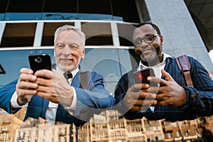 Multiracial men talking and using cellphones while standing by building