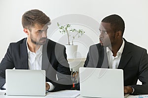 Multiracial office rivals looking at each other, rivalry at work