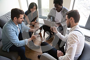 Multiethnic workers sitting in circle using diverse mobile gadgets