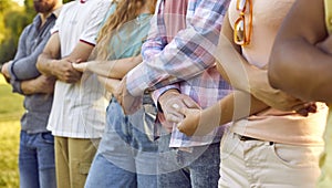 Multiracial people men and woman hold hands as sign of friendship or unity stand in row in park