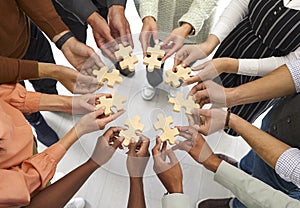 Multiracial people stand in circle and connect wooden pieces of puzzles they hold in their hands.