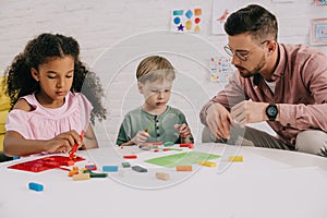 multiracial preschoolers and teacher with plasticine sculpturing figures at table