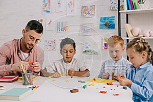multiracial preschoolers and teacher with plasticine sculpturing figures at table