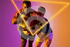 Multiracial rugby male opponents tackling ball by illuminated triangle on gradient background