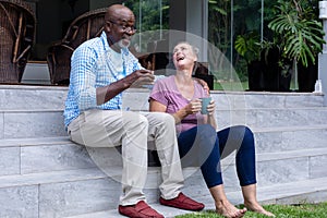 Multiracial senior couple having coffee while sitting on steps outside house