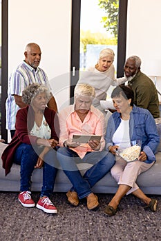 Multiracial senior friends with popcorns watching match over digital tablet in nursing home