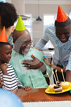 Multiracial senior man wearing party hat looking at cupcakes while celebrating birthday with family