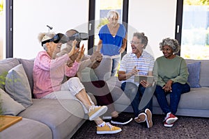 Multiracial seniors with digital pc looking at friends enjoying virtual reality simulator on sofa