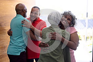 Multiracial seniors embracing and welcoming friends while standing at doorway in nursing home