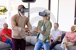 Multiracial seniors looking at excited friends enjoying virtual reality simulator in retirement home