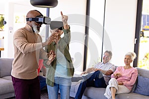 Multiracial seniors looking at friends enjoying virtual reality simulator in nursing home