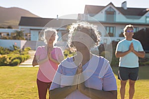 Multiracial seniors meditating while standing against retirement home in yard on sunny day
