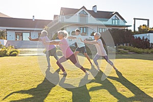 Multiracial seniors stretching while exercising on grassy land against retirement home in yard