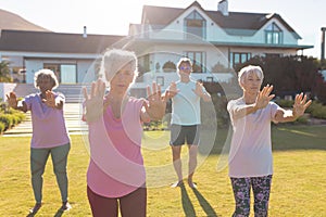 Multiracial seniors stretching hands while exercising in yard against retirement home on sunny day
