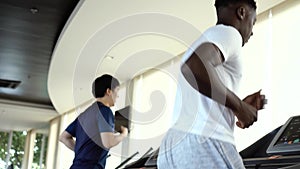 Multiracial sportsmen working out on treadmills in gym on daytime. Multiethnic Asian and African American males running