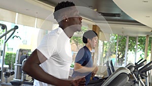 Multiracial sportsmen working out on treadmills in gym on daytime. Multiethnic Asian and African American males running