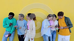 Multiracial students using mobile phones standing together over yellow wall.