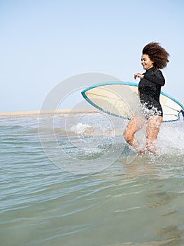 Multiracial surfer girl running to the waves on the beach shore