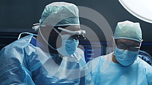 Multiracial team of professional medical surgeons performs the surgical operation in a modern hospital. Doctors are