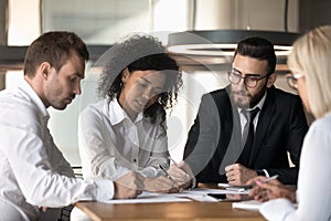 Multiracial team sitting reviewing documents financial stats at group meeting