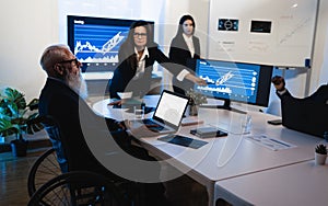 Multiracial trader team making stock market analysis conference inside hedge fund office - Focus on senior man in wheel chair