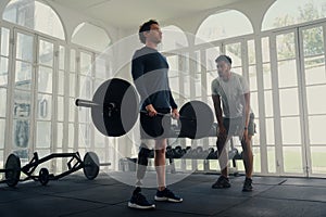 Multiracial trainer doing weightlifting exercises with young man with prosthetic leg at the gym