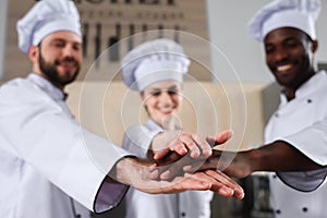 Multiracial tram of cooks stacking hands together