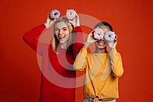 Multiracial two girls laughing while making fun with donuts