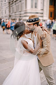 Multiracial wedding couple. African-American bride and Caucasian groom kissing among the crowd in Piazza del Duomo