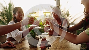 Multiracial women cheering and clinking glasses with wine enjoying dinner party in outdoor sea view cafe. Young