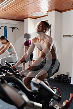 Multiracial young adults doing intense cardio workout on exercise bike at the gym