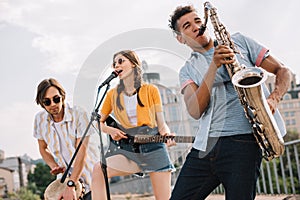 Multiracial young people with guitar djembe and saxophone performing