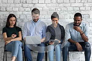 Multiracial young people sit indoor with diverse electronic mobile devices