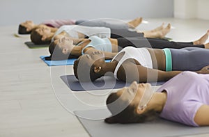 Multiracial young women lie on floor and practice deep breathing exercises in yoga class.