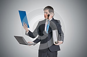 Multitasking man at work is calling with phone, reading report, working with laptop and holding office documents photo