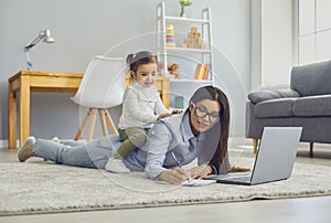 Multitasking for work at home moms. Young woman doing online job on laptop while her daughter sitting on her back