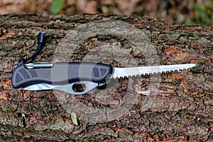 Multitool outdoor equipment, Swiss Soldier`s Knife with extended saw blade on tree trunk in forest
