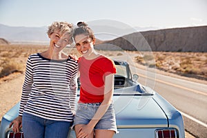 Mum and adult daughter on road trip leaning against the car