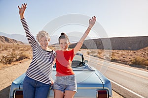 Mum and adult daughter on road trip stand waving to camera