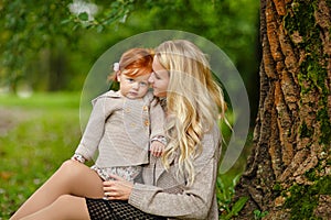 Mum gently embraces the redhead baby girl on autumn forest background